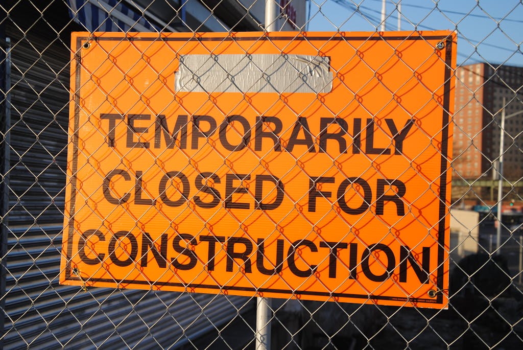 Orange sign behind fence reading 'Temporarily Closed for Construction' at site.